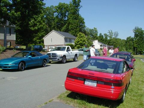1994 Ford Probe - Several cars and a pickup truck are parked on a residential street on a sunny day.