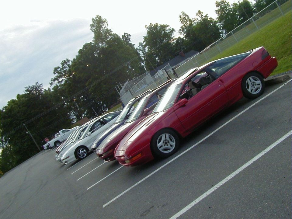 Red coupe with a sloping rear, parked diagonally in a lot with other cars