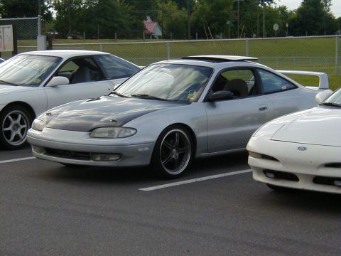 1994 Ford Probe - Silver coupe with aftermarket hood and wheels parked in a lot.