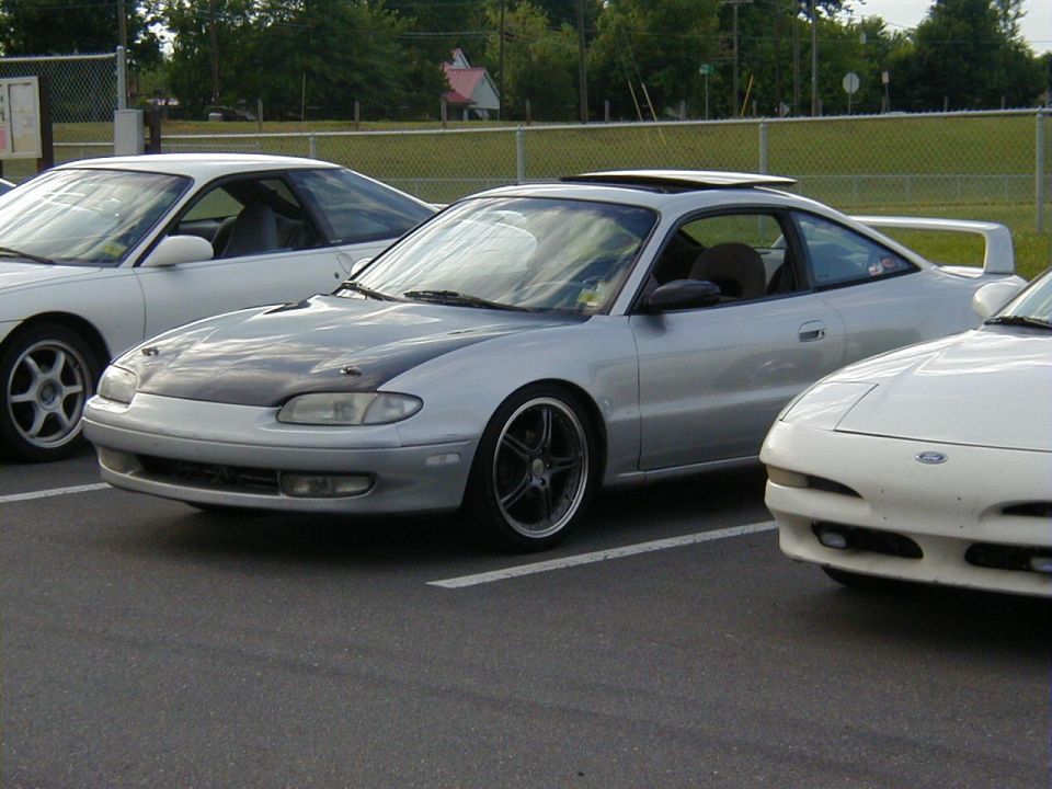Silver coupe with aftermarket hood and wheels parked next to other cars