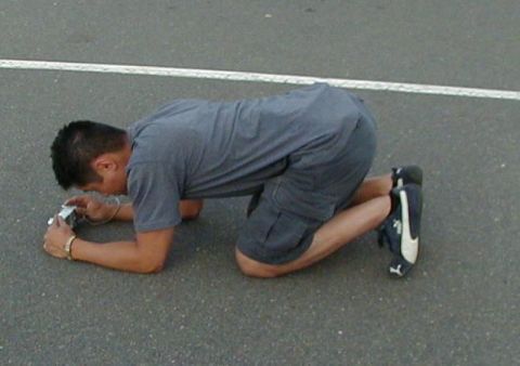 1994 Ford Probe - A man kneels on asphalt, focusing his camera on an unseen vehicle.