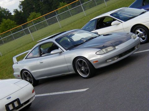1994 Ford Probe - A silver coupe with a contrasting black hood and a prominent rear spoiler is parked alongside other vehicles.
