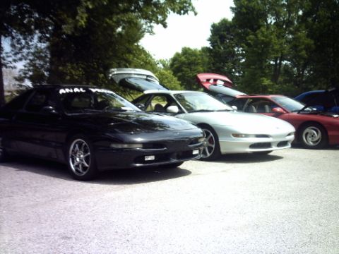 1995 Ford Probe - A line of Ford Probes, including a black 1995 model with a custom windshield banner, are parked outdoors.