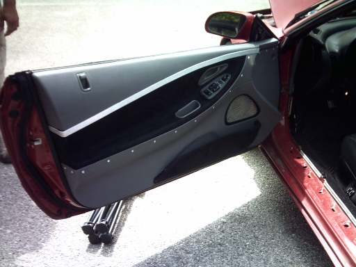 Open driver's door of red coupe showing custom gray and black door panel with metal trim and switches