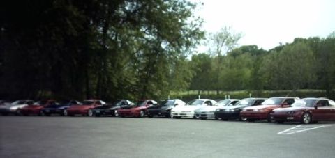 1995 Ford Probe - A line of cars is parked in an outdoor lot with trees visible behind them.