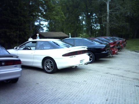 1995 Ford Probe - A line of Ford Probes are parked on a paved surface with trees in the background.