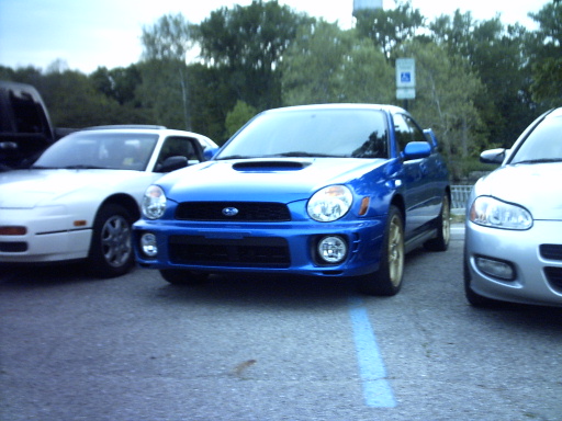 Blue Subaru Impreza WRX with gold wheels, front view, parked in a lot