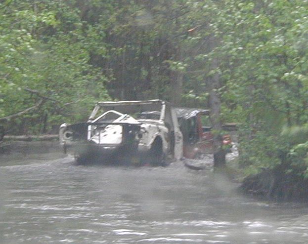 off-road vehicle stuck in muddy water with trees around