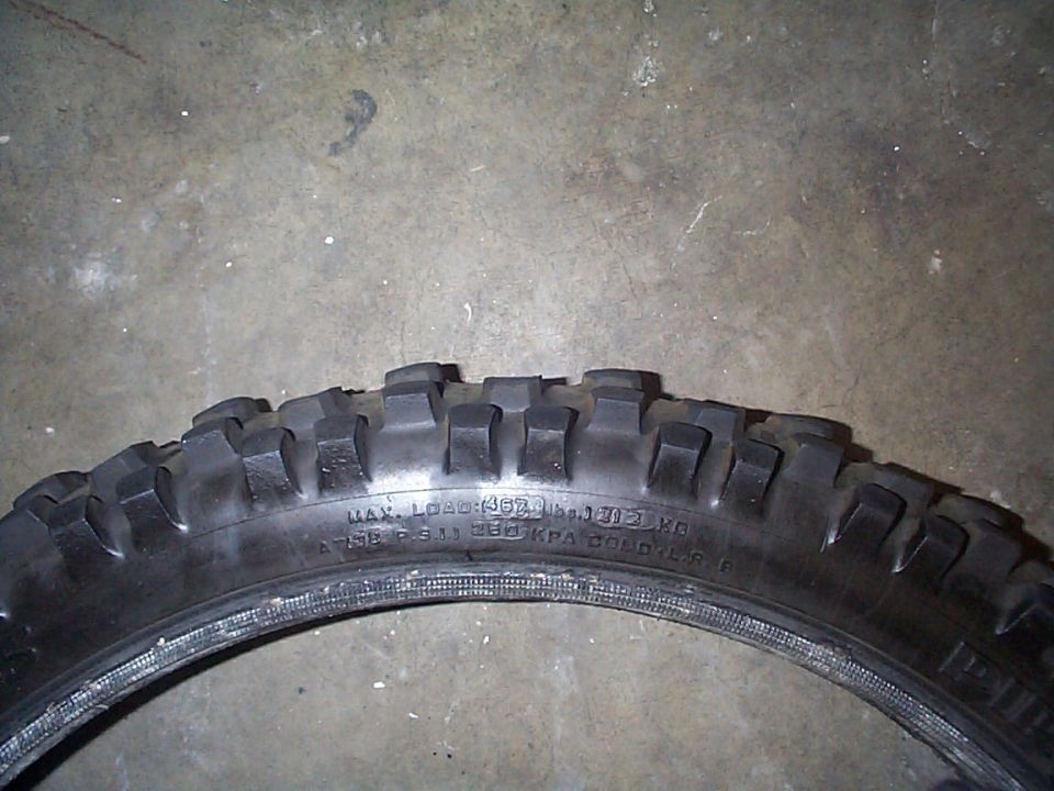 Motorcycle tire with knobby tread, showing sidewall markings for load and pressure