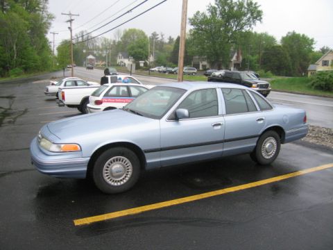 2001 Ford Crown Victoria - A light blue 2001 Ford Crown Victoria sedan is parked in a lot with other vehicles.