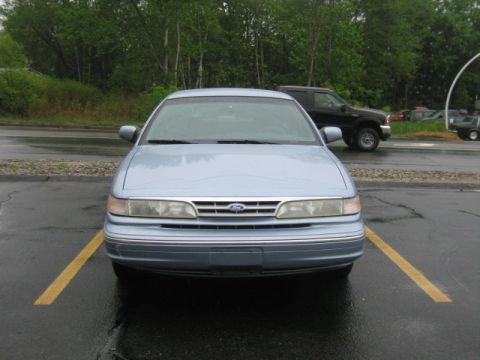 2001 Ford Crown Victoria - A light blue sedan is parked in a lot on a cloudy day. Another vehicle is parked behind it.
