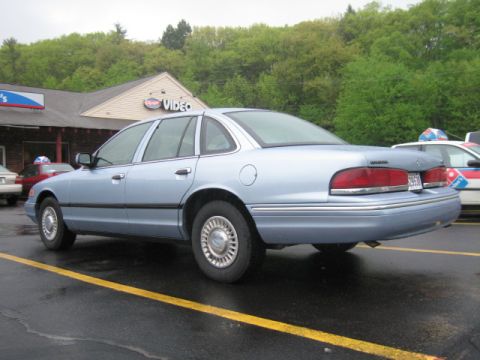 2001 Ford Crown Victoria - A light blue 2001 Ford Crown Victoria sedan is parked in a lot next to another vehicle.