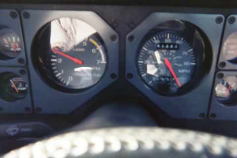 1985 Ford Mustang - Close-up of a Fox-body Ford Mustang instrument cluster shot over the rim of a laced steering wheel cover, showing the 7,000-rpm tachometer…