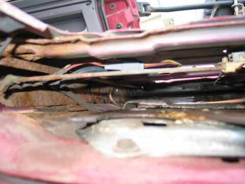 1995 Ford Bronco - Close-up view of severe rust and exposed wiring beneath the seat of a red vehicle.