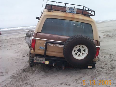 1983 Ford Bronco - Ford Bronco stuck in sand on beach with spare tire mounted on rear.
