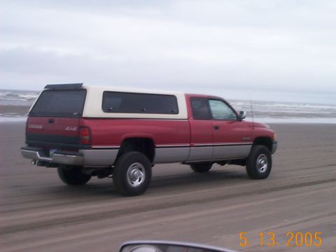 1983 Ford Bronco - Dodge pickup truck with a camper shell on a beach under an overcast sky.
