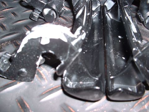 1978 Ford Mustang II - Close-up of a black plastic car part with white paint splatters, resting on a textured metal surface.
