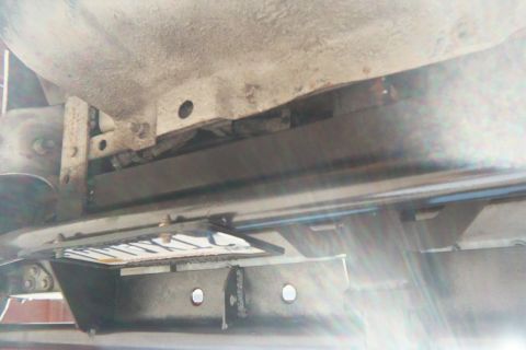 1990 Ford Bronco - Looking up at a vehicle's undercarriage showing a transmission pan, crossmember and dusty frame rails.