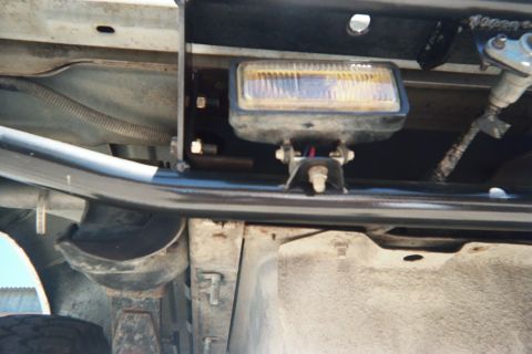 1990 Ford Bronco - Underside view of a rectangular auxiliary driving light wired and mounted behind a black tube bumper on a vehicle.