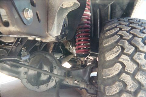 1990 Ford Bronco - Close-up of a vehicle's front suspension showing a red coil-over spring, differential housing, steering linkage and a mud tire.