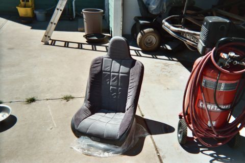 1990 Ford Bronco - black-and-gray suspension-style racing bucket seat rests on a driveway beside a red Craftsman air compressor and tires.