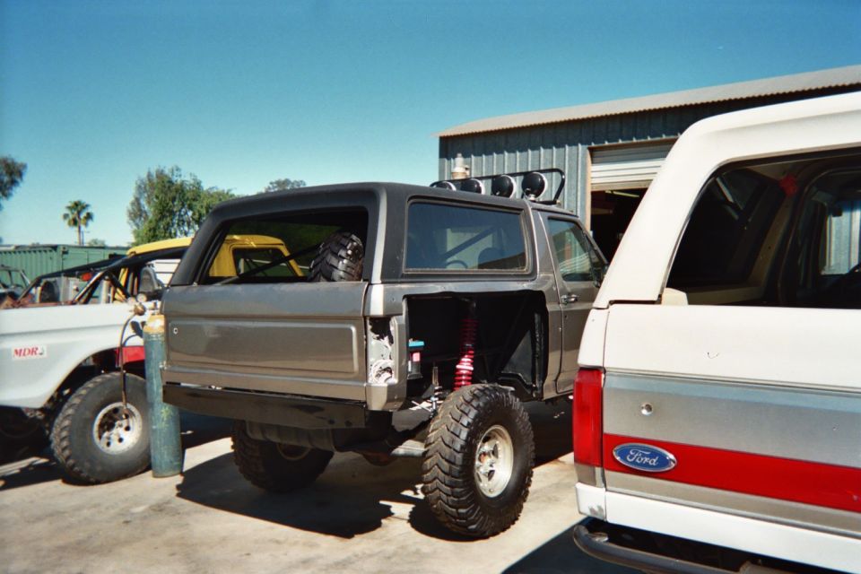 Rear of a gray cut-down off-road SUV with coilovers beside a white Ford Bronco