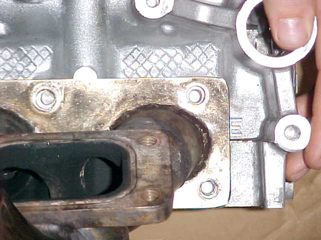 Close-up of an exhaust manifold bolted to a silver engine block. A hand is visible on the right
