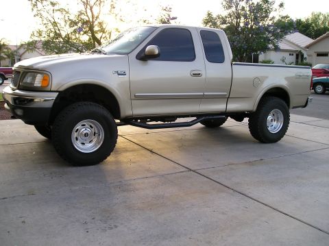 1999 Ford F-150 - Side view of a lifted 1999 Ford F-150 pickup truck with custom wheels and running boards.