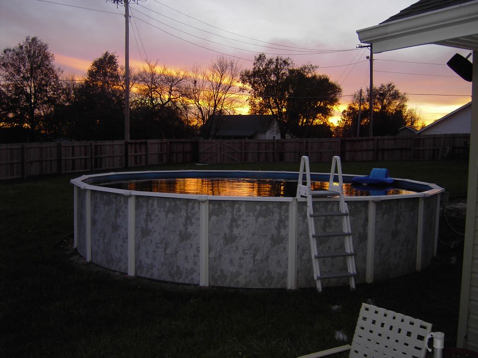 Above-ground backyard pool with white ladder at sunset behind a wood fence