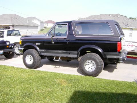 1991 Ford Bronco - This black 1991 Ford Bronco features a two-tone gray trim and a removable hardtop, seen parked next to other vehicles.