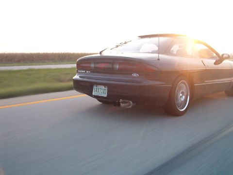 1995 Ford Probe - Rear view of a black 1995 Ford Probe on the highway during sunset.
