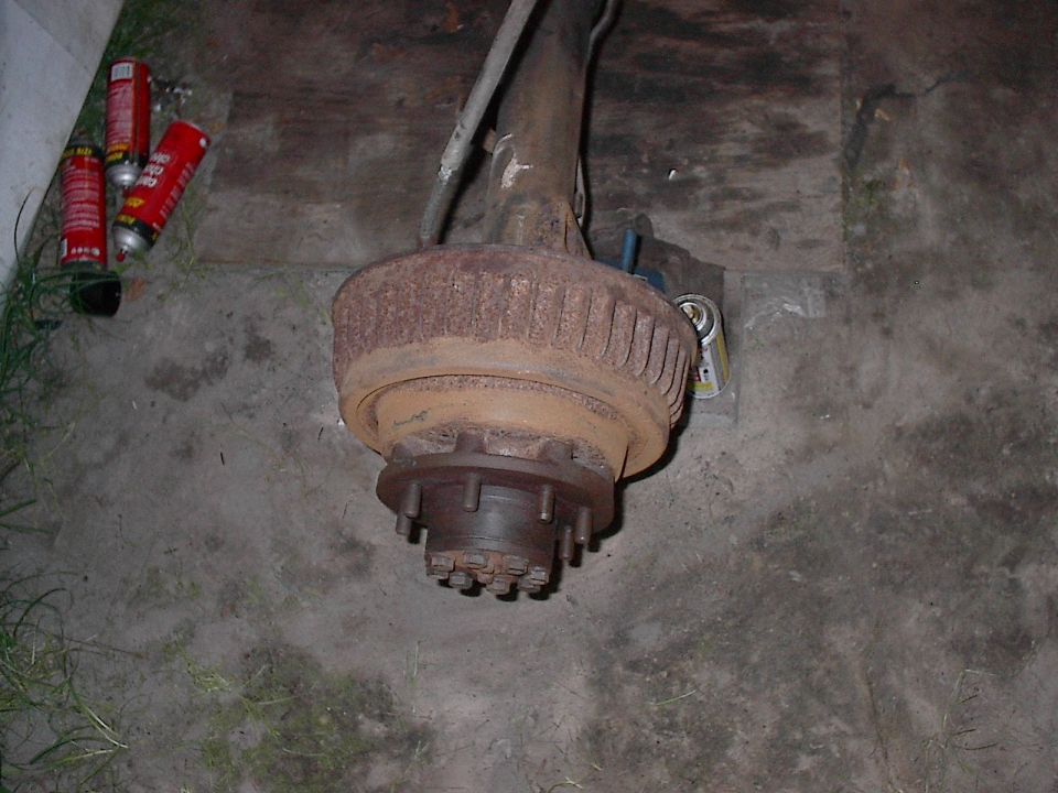 Rear axle assembly with drum brake, sitting on concrete. Three spray cans nearby