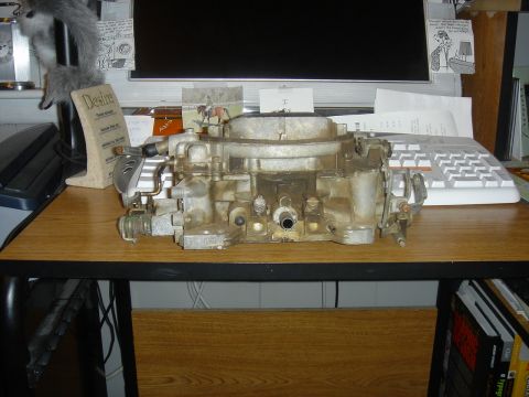 1986 Ford Mustang - A close-up view of a used carburetor, likely for an older vehicle, rests on a wooden desk.