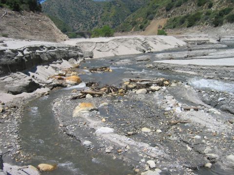 1985 Ford Bronco - A dry riverbed with scattered rocks and debris, leading towards a distant bridge.