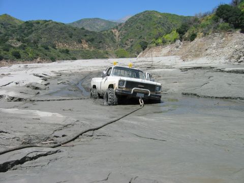 1985 Ford Bronco - A white GMC pickup truck is stuck in thick mud with a tow rope attached to its front.