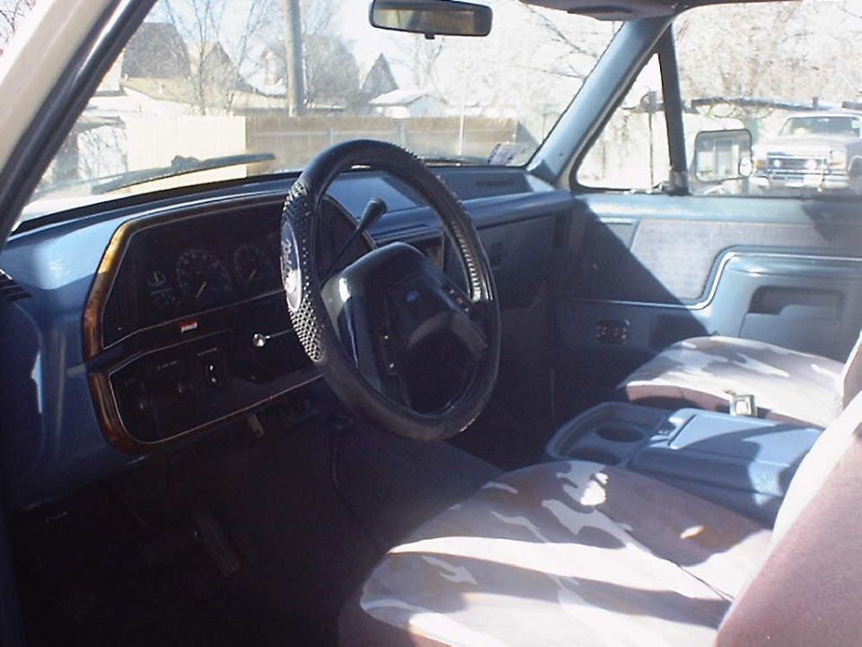 Blue Ford truck interior with woodgrain dash, laced steering wheel cover and camo seat covers