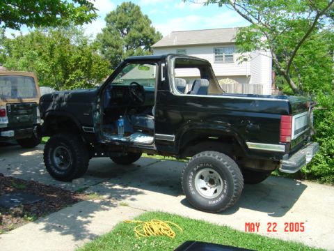 1986 Ford Bronco - Black Ford Bronco with its doors removed, parked next to another vehicle in a driveway.