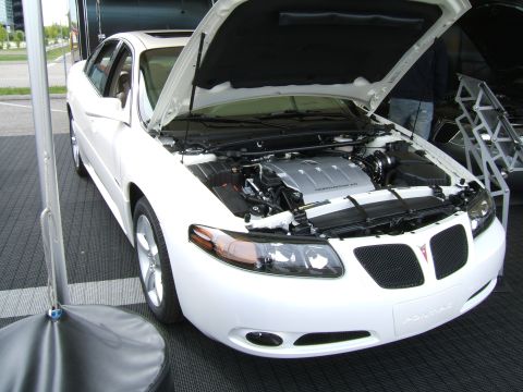 1998 Ford Taurus - White 2004 Pontiac Grand Prix with hood open, displaying the engine and front grille. The vehicle is on display.