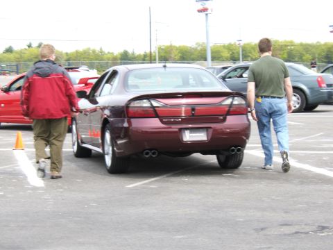 1998 Ford Taurus - A maroon sedan is parked in a lot with other vehicles and people nearby.