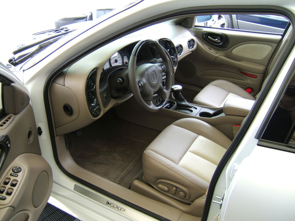 Car interior with tan seats, dashboard, steering wheel, and center console. "GXP" emblem visible on door sill