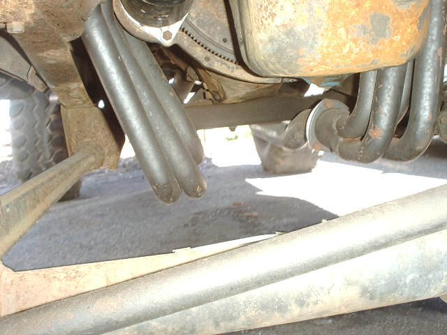 Close-up under a truck of dual exhaust pipes, leaf springs and rusty crossmember