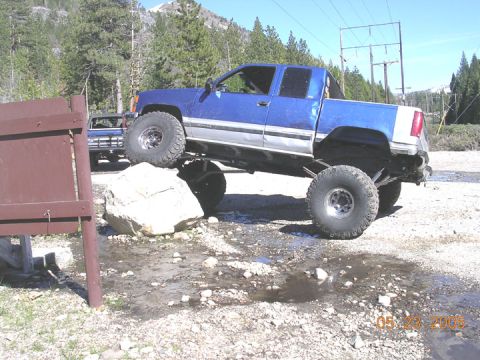 1994 Ford Bronco - A blue pickup truck navigates a rocky terrain with a second vehicle visible in the background.