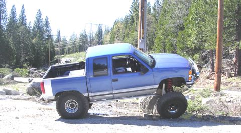 1994 Ford Bronco - Blue pickup truck with lifted suspension is parked on rocks off-road.