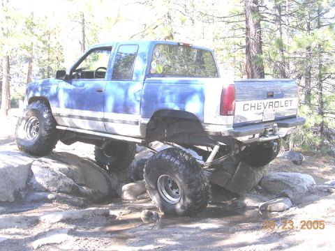 1994 Ford Bronco - This Chevrolet pickup truck is shown off-roading on a rocky terrain with trees in the background.