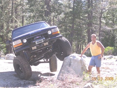 1994 Ford Bronco - A black Ford Bronco navigates an off-road obstacle with a man observing.