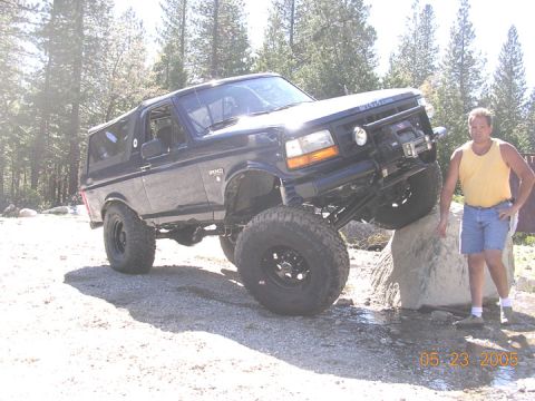 1994 Ford Bronco - A man stands next to a black 1994 Ford Bronco as it navigates rocky terrain.