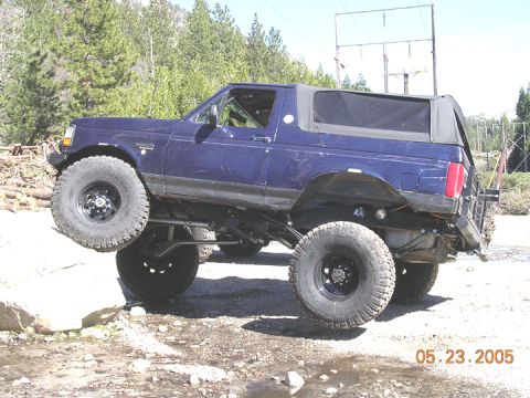 1994 Ford Bronco - A blue 1994 Ford Bronco navigates rocky terrain with its suspension significantly lifted.