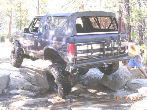 1994 Ford Bronco - This Ford Bronco is tackling a rocky trail, with a person visible near the rear of the vehicle.