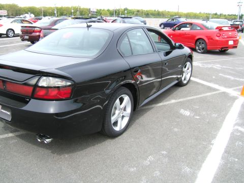 1998 Ford Taurus - A black Pontiac sedan is parked in a lot with other vehicles, including a red coupe in the background.