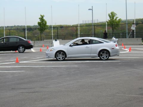 1998 Ford Taurus - A silver coupe navigates a course marked by orange cones, with another car visible in the background.